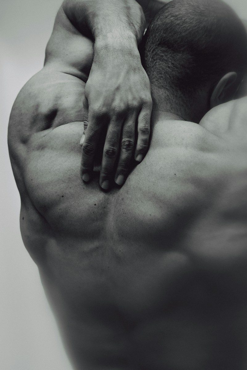 A person with a muscular back reaching a hand to their neck