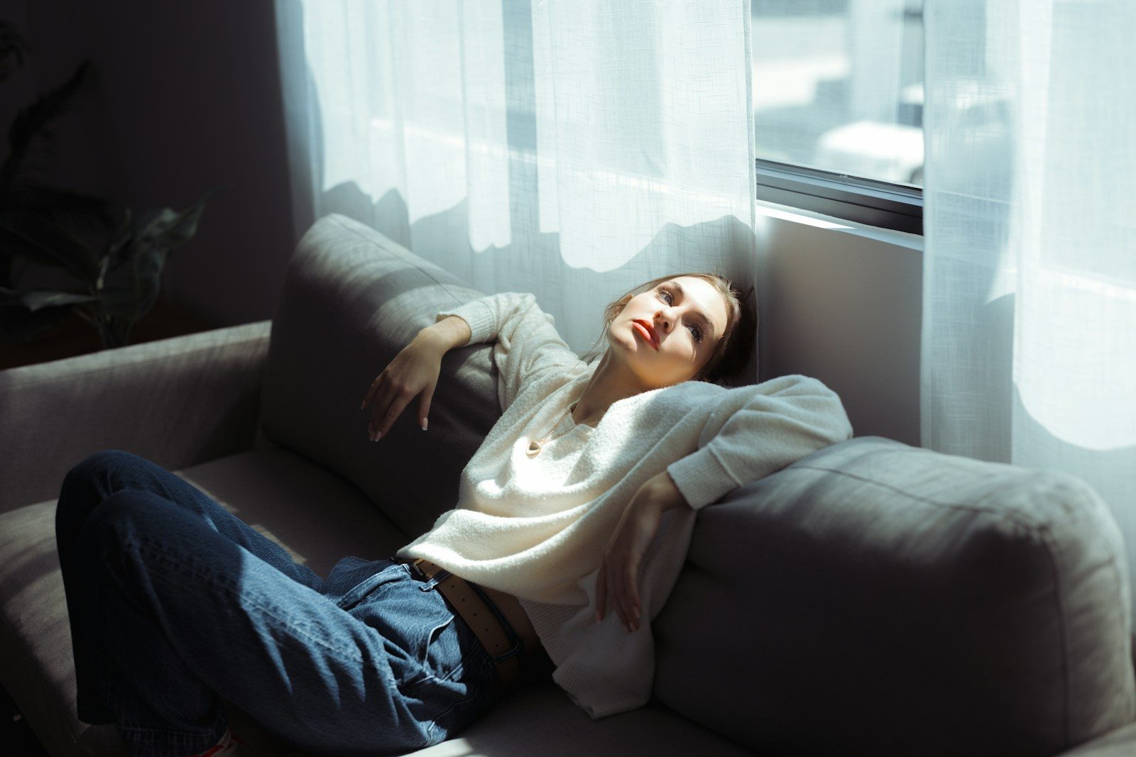 A woman in a white sweater and blue jeans reclining on a grey sofa